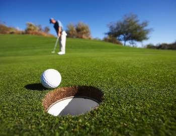 close up of a golf ball about to go in the hole with the player in the background 